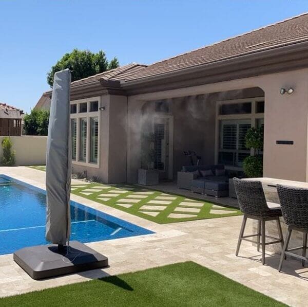 Misting system installation near a swimming pool in a residential backyard, showcasing a modern home with outdoor seating and landscaping.