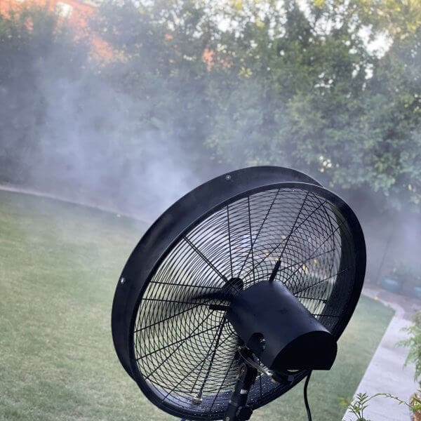Misting system installation in residential setting, showcasing outdoor fan with misting feature, surrounded by greenery.