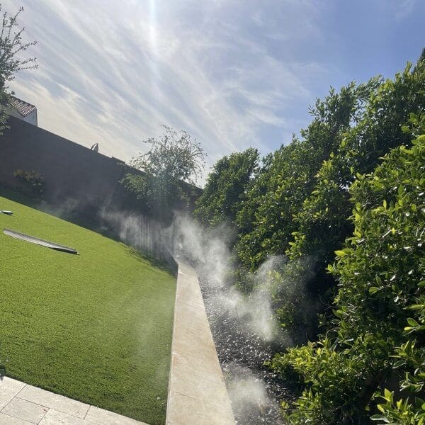 Misting system installation in residential backyard, showcasing mist effect near greenery and artificial turf, illustrating Second Opinion Plumbing's expertise in outdoor cooling solutions.